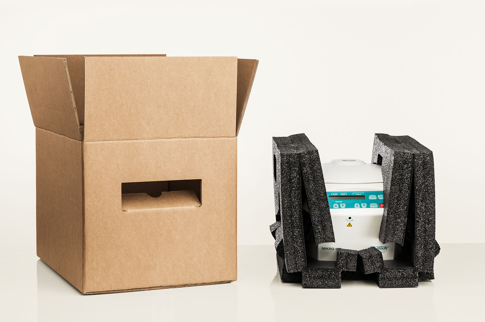 Eine Zentrifuge ist in einem faltbaren Polster aus schwarzem Recyclingschaum eingepackt. Der passende Karton steht bereit.